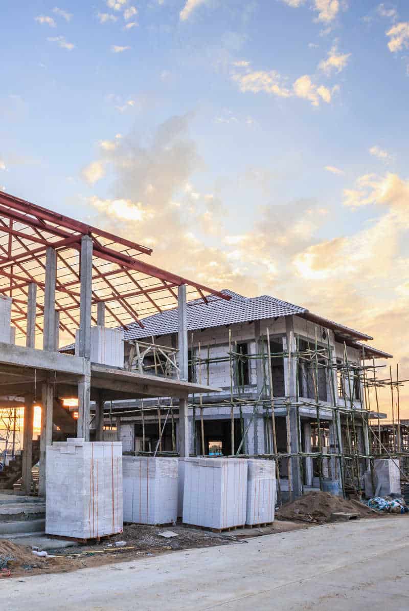 An active construction site with partially built structures, exposed materials, and scaffolding under a sunset sky, highlighting the need for security to prevent theft and unauthorized access.