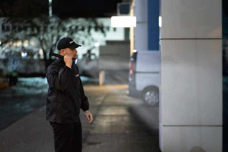 A security guard in a black uniform patrolling a commercial property at night, holding a flashlight to inspect the premises for potential security threats.