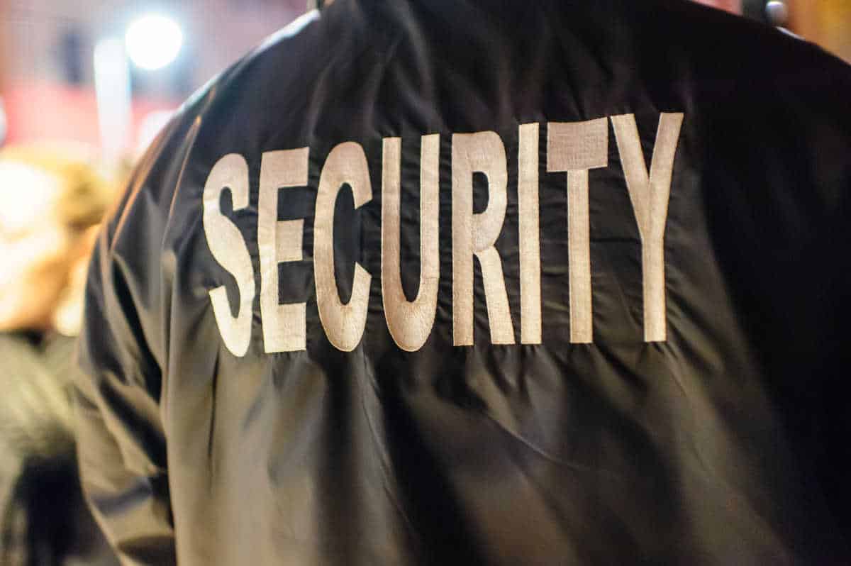 Close-up of a security guard wearing a black jacket with 'SECURITY' printed on the back, monitoring a public area to ensure safety and protection.