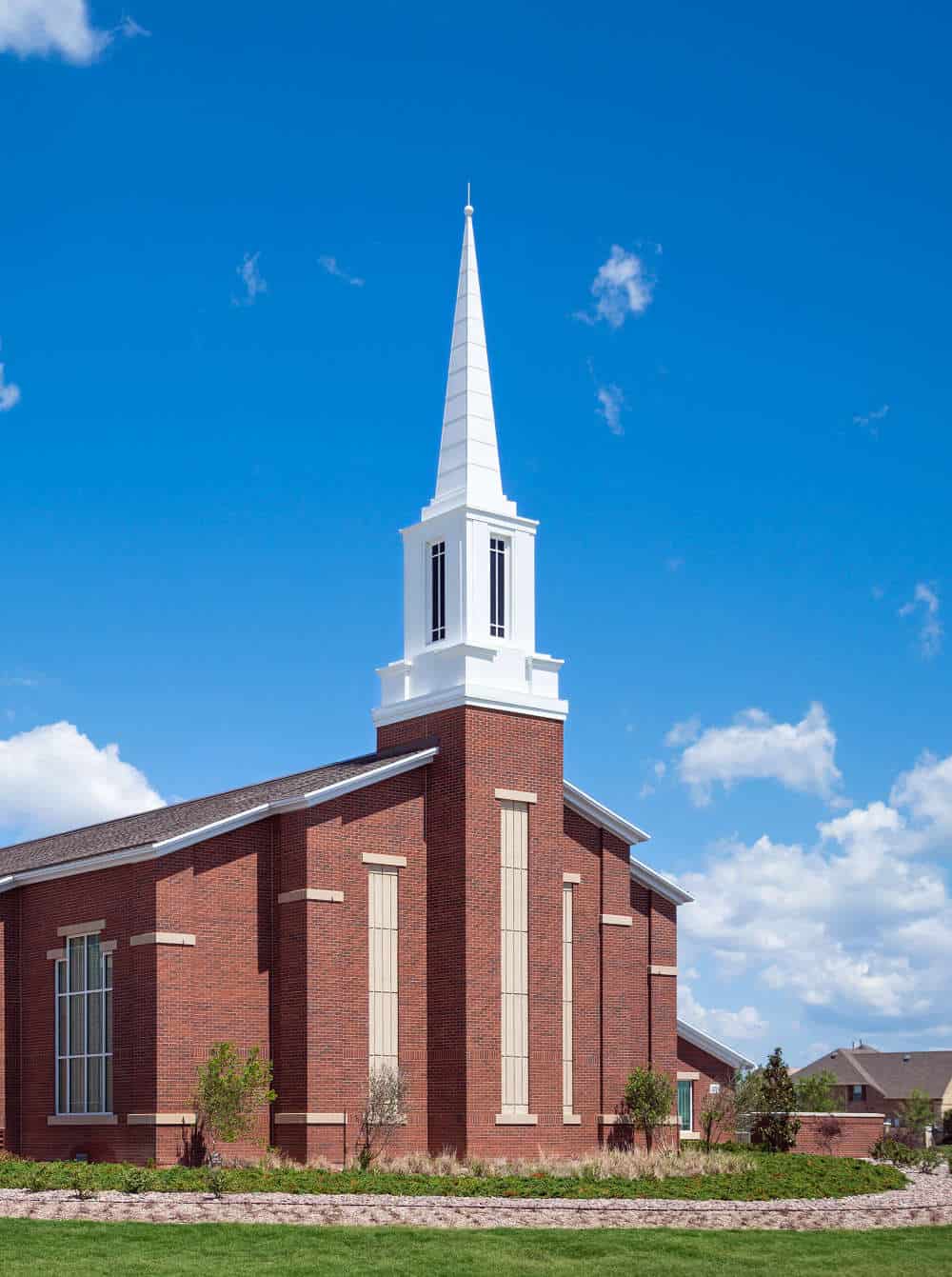 Brick Church Building with Steeple on a Sunny Day A red brick church with a tall white steeple, set against a bright blue sky with scattered clouds and surrounded by green landscaping.