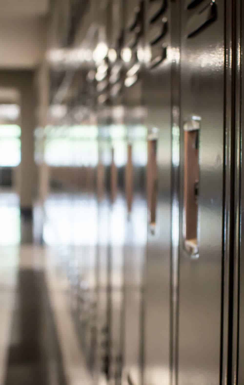 Empty School Hallway with Lockers Row of metal lockers lining an empty school hallway with polished floors and natural light coming through the windows at the end of the corridor.