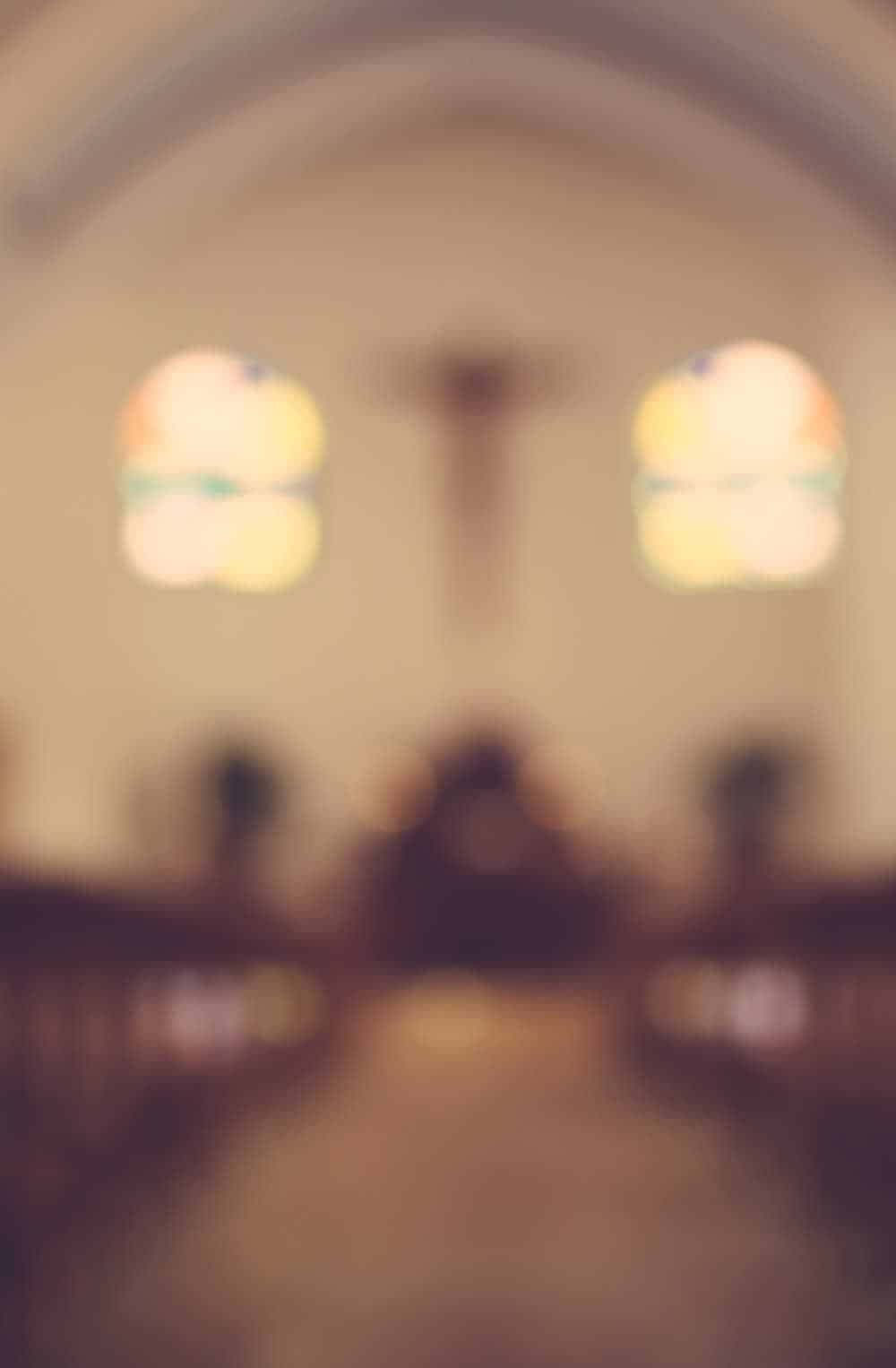 Peaceful Interior of a Church with Stained Glass Windows Blurred view of a church interior featuring wooden pews, arched ceilings, and colorful stained glass windows with a cross at the altar.